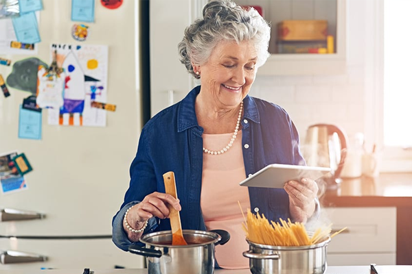 elderly lady reading tablet while cooking